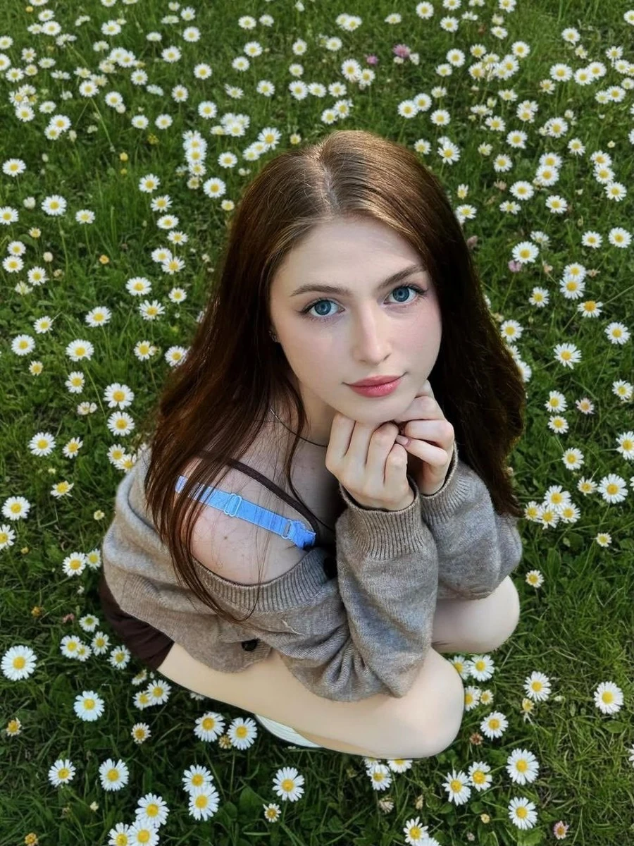 A soft, natural portrait of a young woman sitting in a lush green field f...