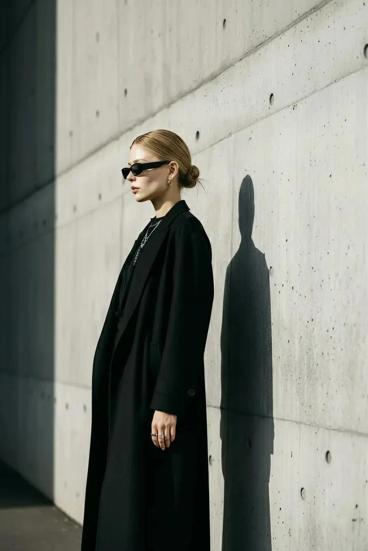 A stylish woman standing against a modern concrete wall, wearing an all-b...