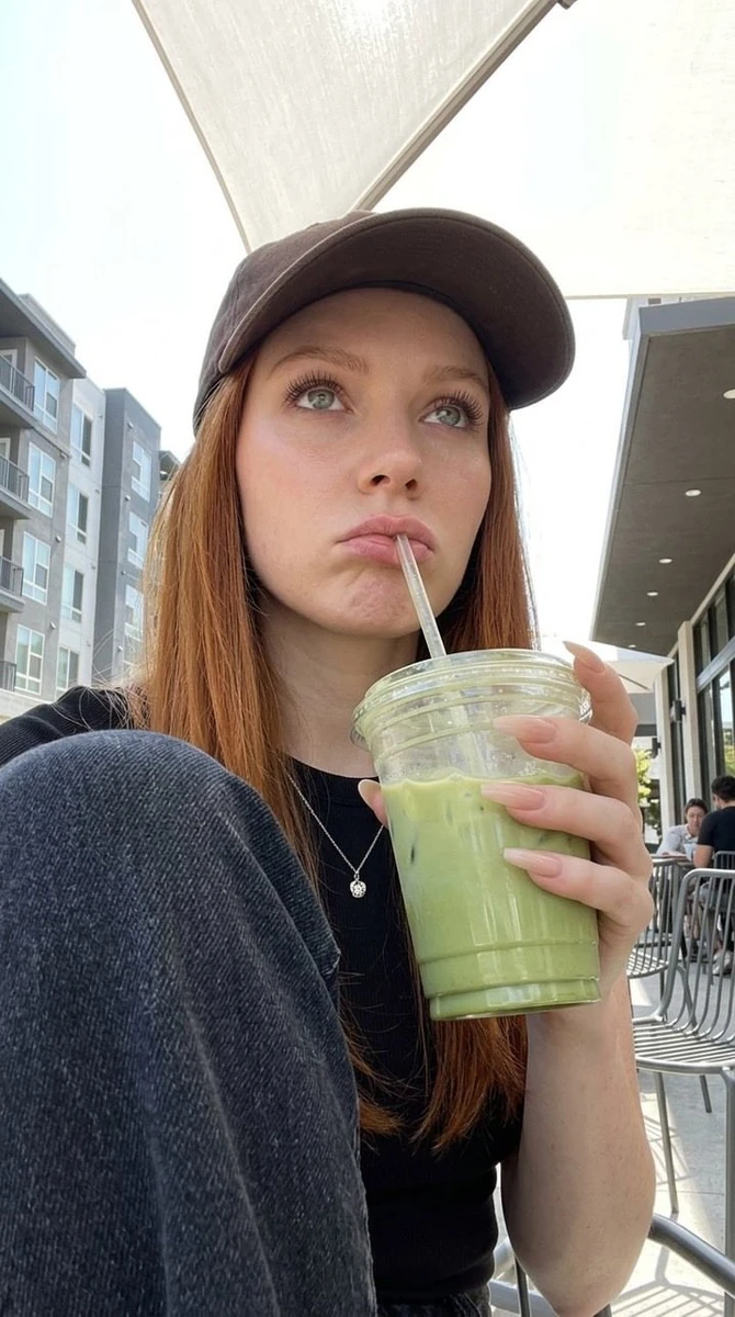 A candid portrait of a young woman sitting outdoors at a modern café, wea...