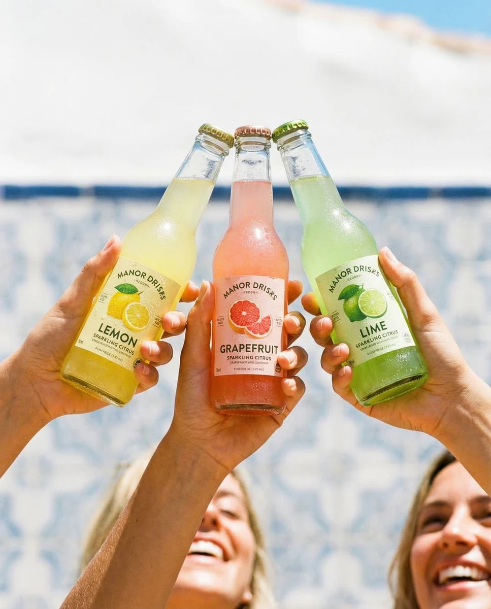 Three hands holding colorful glass soda bottles (lemon, grapefruit, lime)...