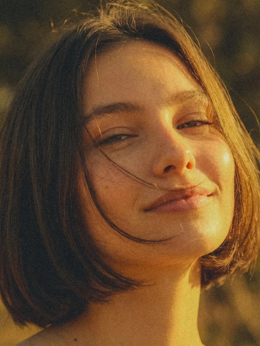 Close-up portrait of a young woman with short hair, subtle smile, face il...