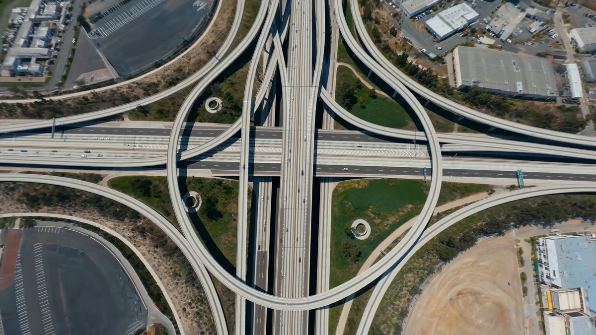 Rapid zoom down elevated freeways into a daylight cityscape with bending-...