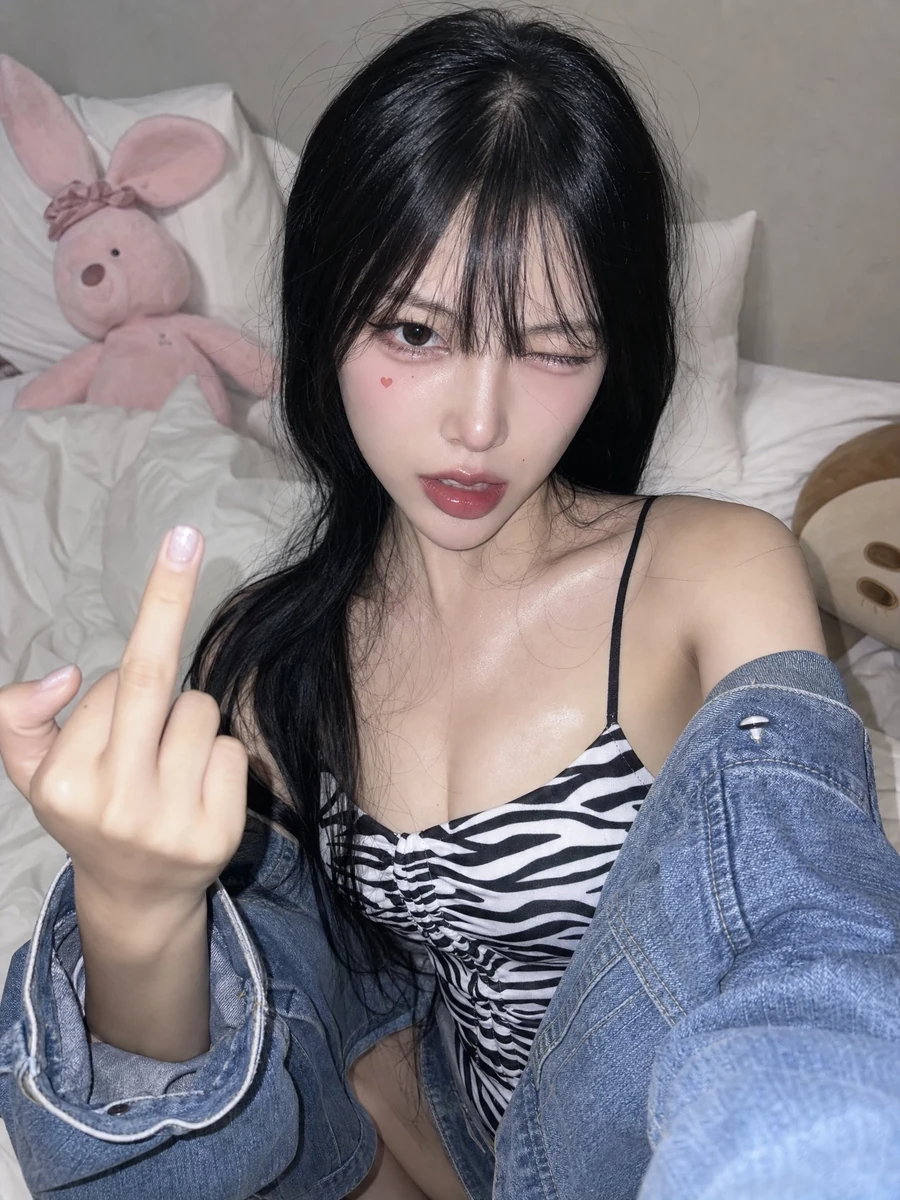 A high-angle front-camera phone selfie of a young woman in her 20s sittin...