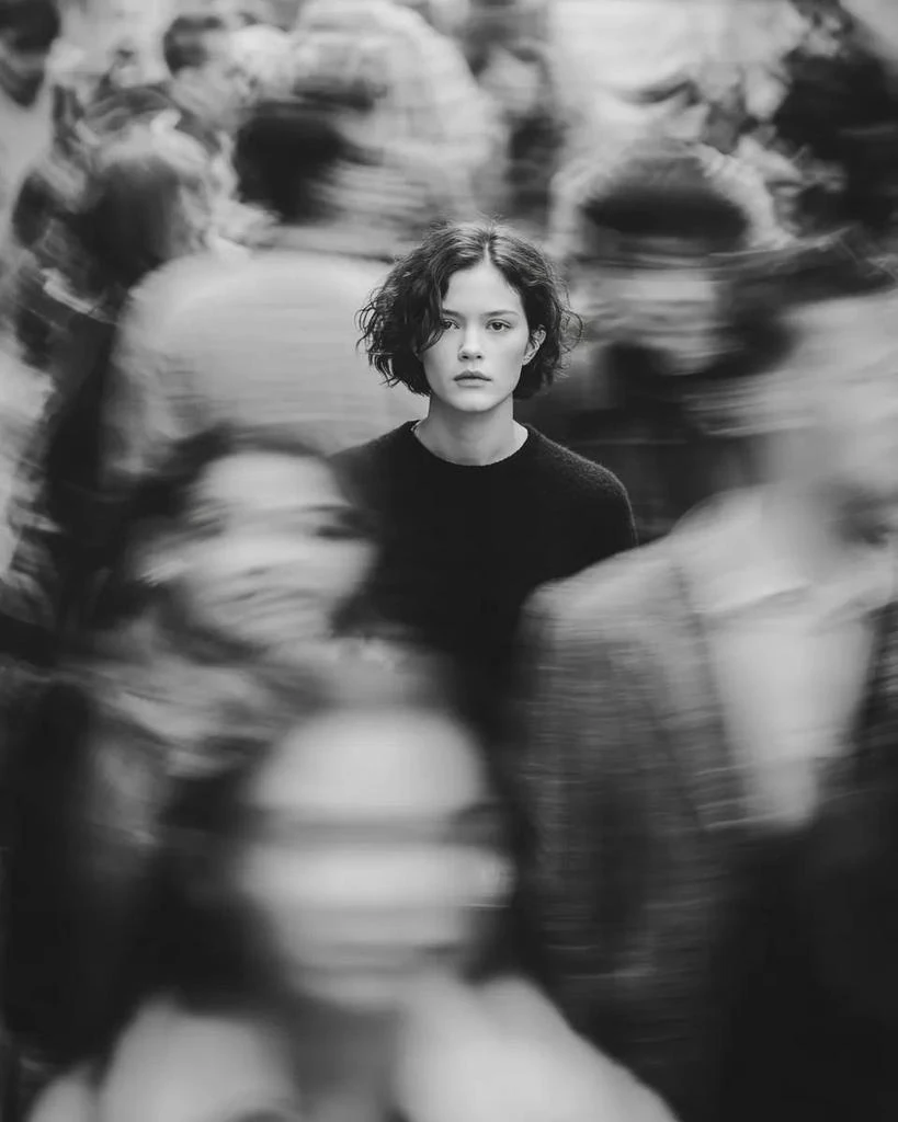 Black and white cinematic portrait of a young woman standing still in the...
