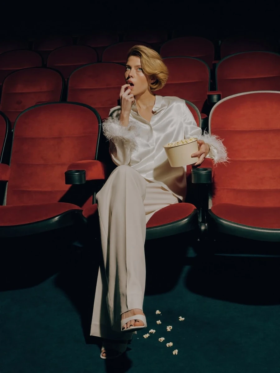 Elegant fashion editorial of a stylish woman sitting alone in a dark movi...
